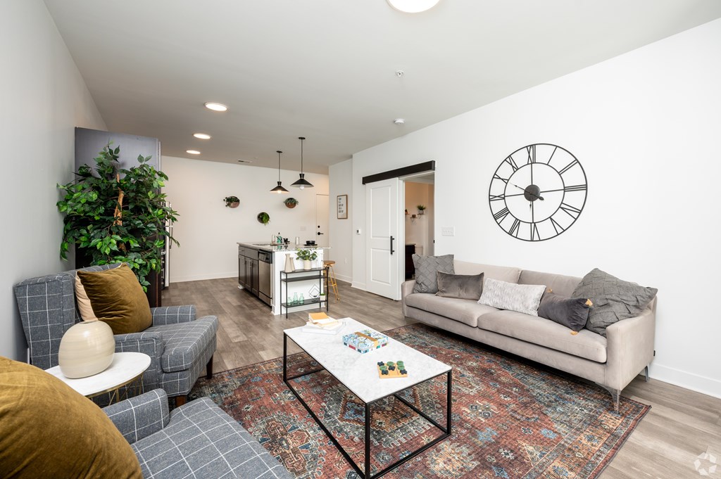 A living room with a grey couch, a white coffee table, and a large clock on the wall.