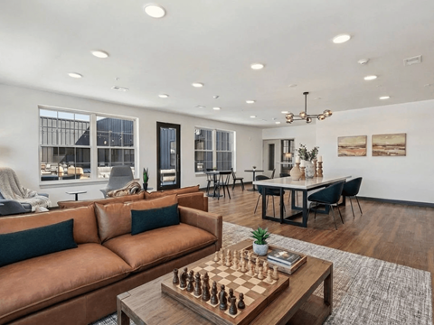 A living room with a brown leather couch and a chess board on the coffee table.
