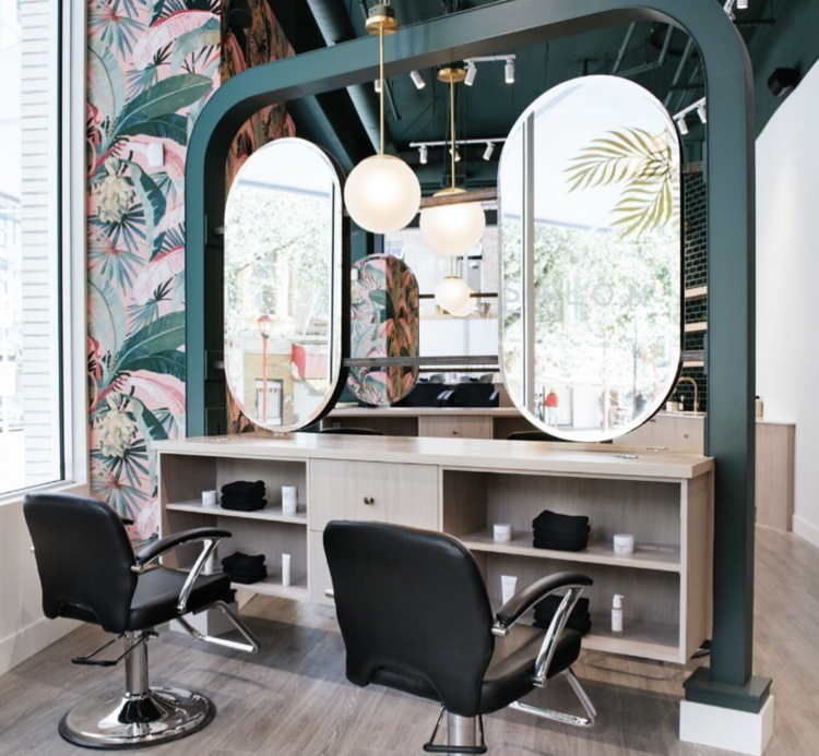 a hair salon with two black chairs and three large mirrors
