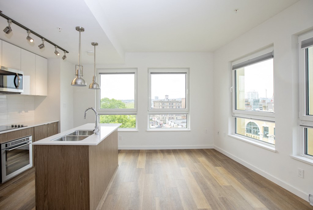 an empty living room with a kitchen and a large window