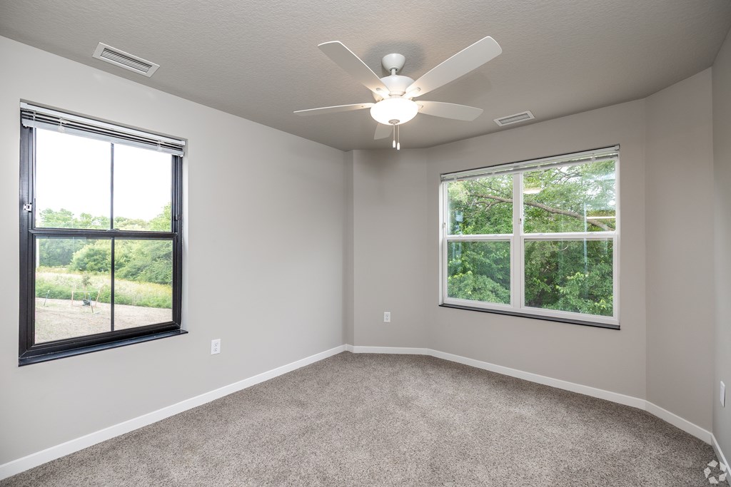 A room with a ceiling fan and two windows.