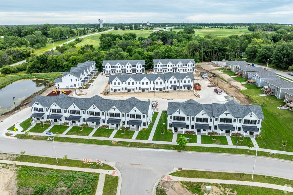 A large, modern building complex with multiple white and grey buildings, surrounded by greenery and a body of water.