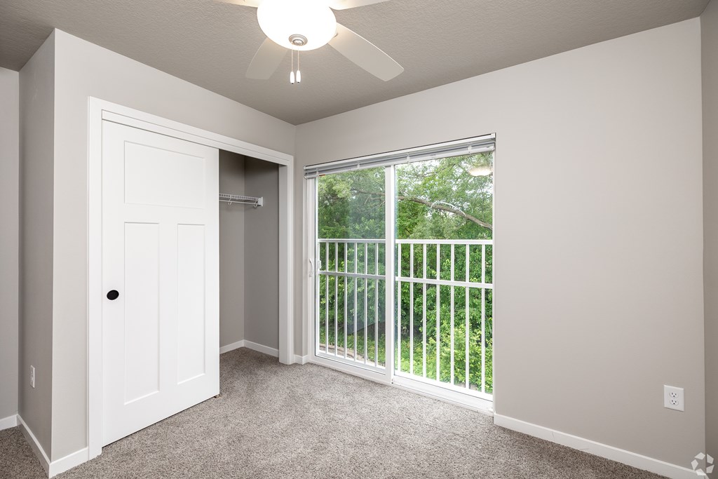 A room with a white door and a window with a view of a green area outside.