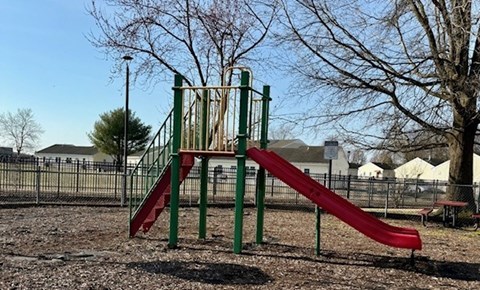 A red slide on a playground with a green metal frame.