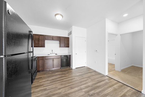A black refrigerator is on the left in a kitchen with wooden floors.