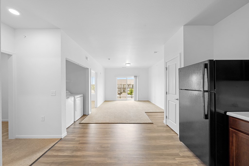 A black refrigerator is in a kitchen with white walls and wood floors. at Union at the Loop, Lawrence, KS