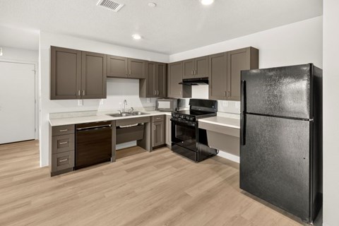 A black refrigerator stands in a kitchen with wooden floors and white walls.