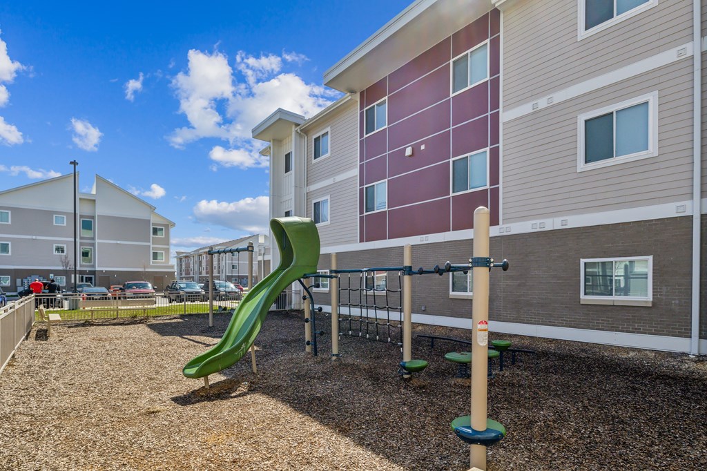 A playground with a green slide in front of a building at Union at 16th, Indianapolis, IN
