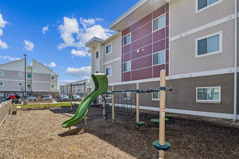 A playground with a green slide in front of a building.