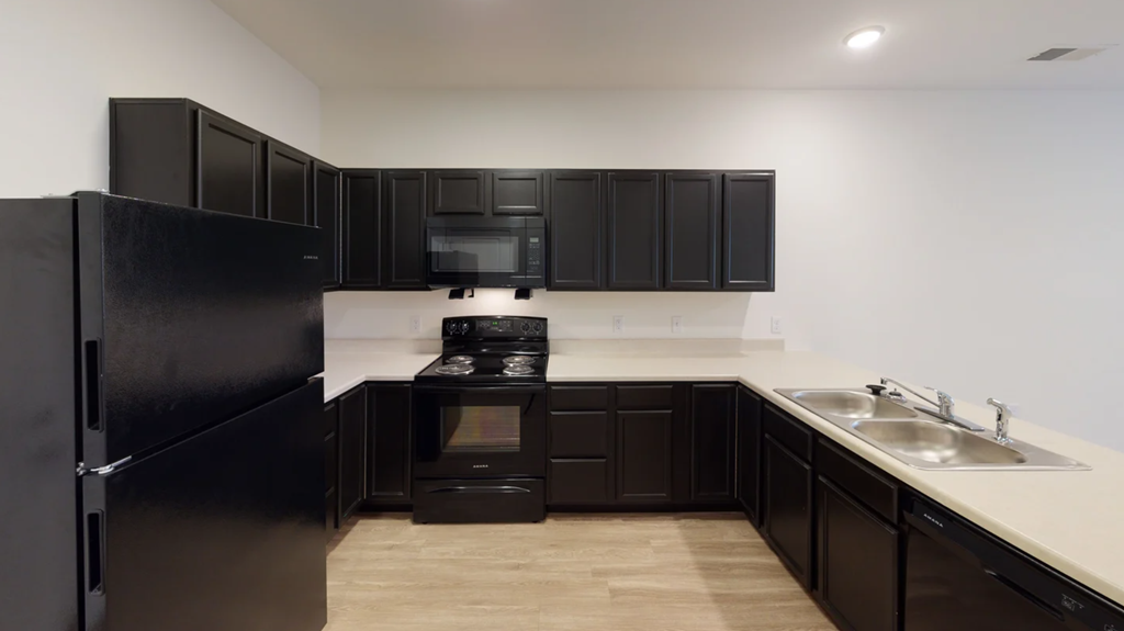 A black fridge and microwave in a kitchen with wooden floors at Union at 16th, Indiana