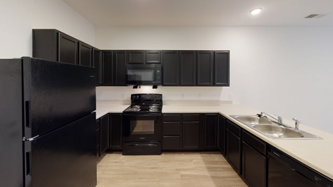 A black fridge and microwave in a kitchen with wooden floors.