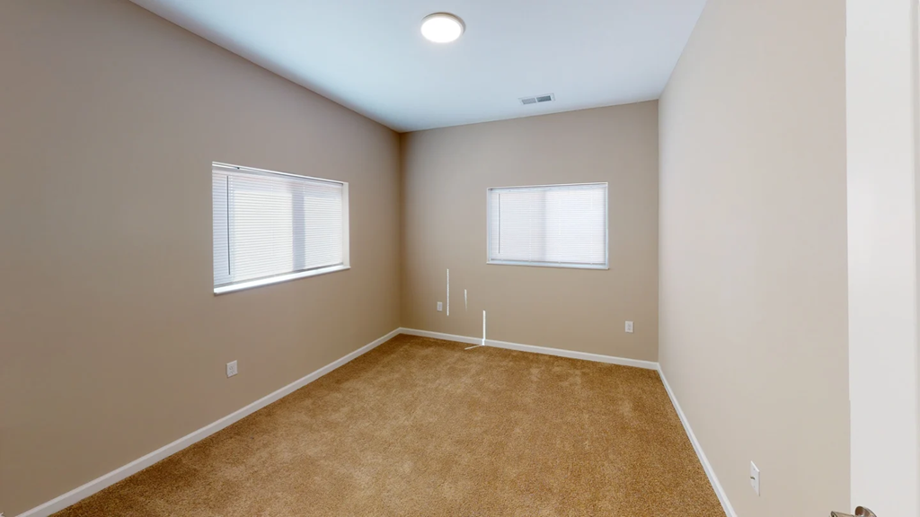 A room with a carpeted floor and two windows at Union at 16th, Indianapolis, IN 46222