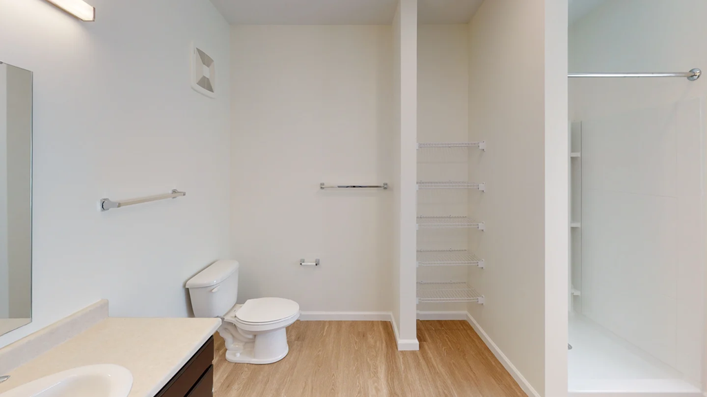 A white toilet sits in a small bathroom with a sink and a mirror.at Union at 16th, Indiana