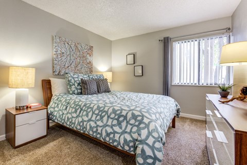 A bedroom with a bed, nightstand, and window at The Ranch at Bear Creek Apartments, Lakewood, CO