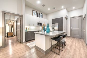 A modern kitchen with a bar stool and a fridge.at The Bridge at McKinney, McKinney, TX