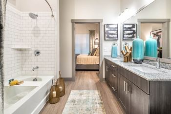 A bathroom with a white tub and a shower with a glass door.at The Bridge at McKinney, McKinney, 75069