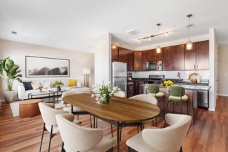 a living and dining room area with a kitchen in the background and a large table in the at West 130, West Hempstead New York