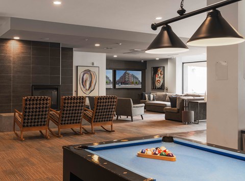 A pool table with a blue cloth and a pool game set up in a room with a fireplace and a couch at Regatta Sloans Lake Apartments, Colorado, 80204