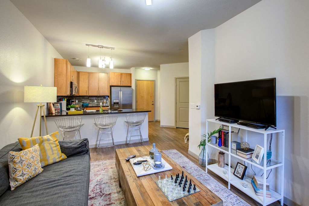 A modern living room with a grey couch, a wooden coffee table, and a flat screen TV on a white stand at Regatta Sloans Lake Apartments, Denver, CO