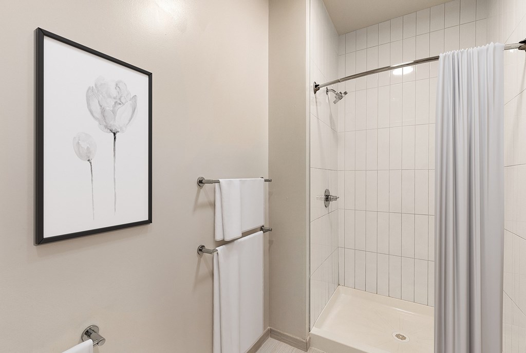 A white bathroom with a shower curtain and a framed picture of a flower at RiDE at RiNo Apartments, Colorado, 80216