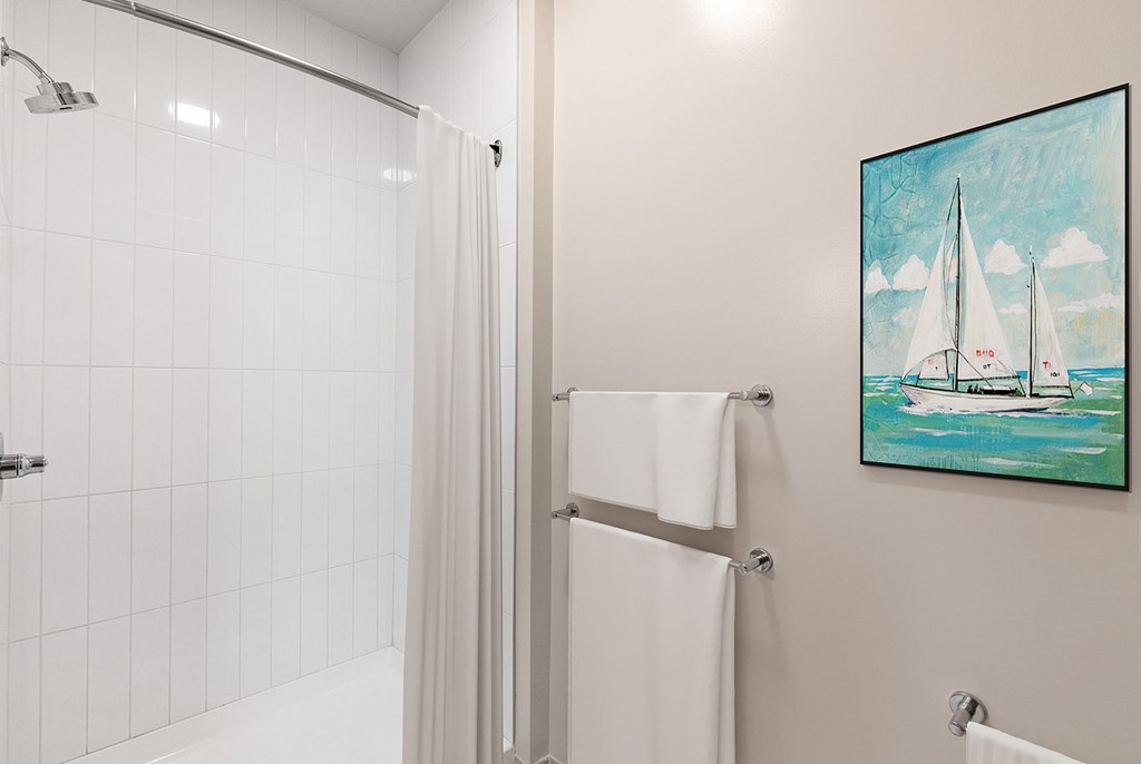 A bathroom with a shower and a painting of a sailboat on the wall at RiDE at RiNo Apartments, Denver