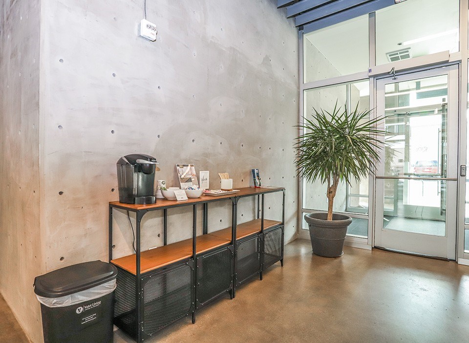 A concrete wall with a black trash can and a wooden shelf with a plant on it at RiDE at RiNo Apartments, Denver 80216