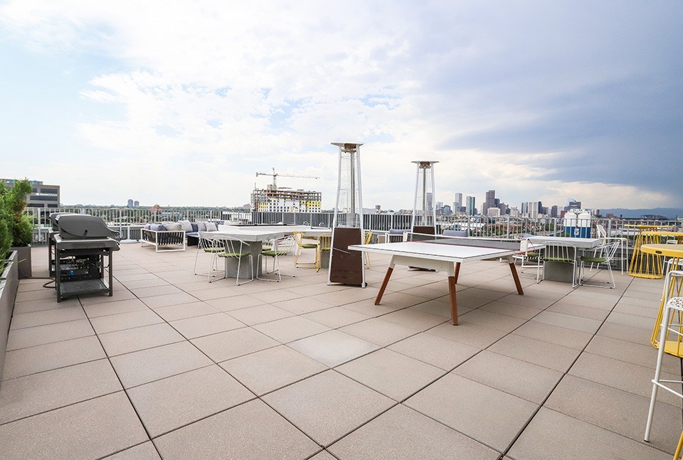 A rooftop patio with a table and chairs overlooking a city skyline at RiDE at RiNo Apartments, Denver, Colorado