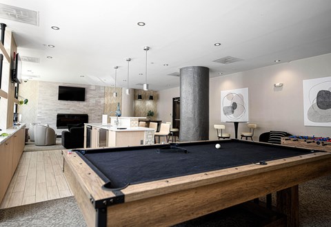 A pool table is in the middle of a room with a bar and a television.