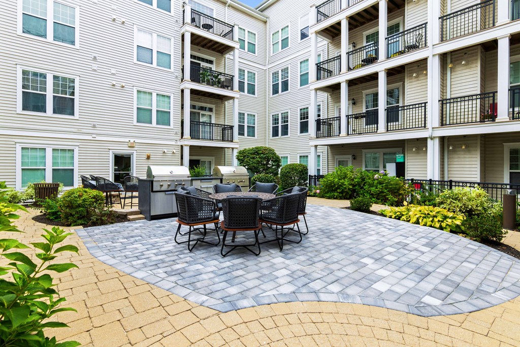 a patio with a grill and a table and chairs in front of an apartment building at Metro 303, Hempstead, NY 11550