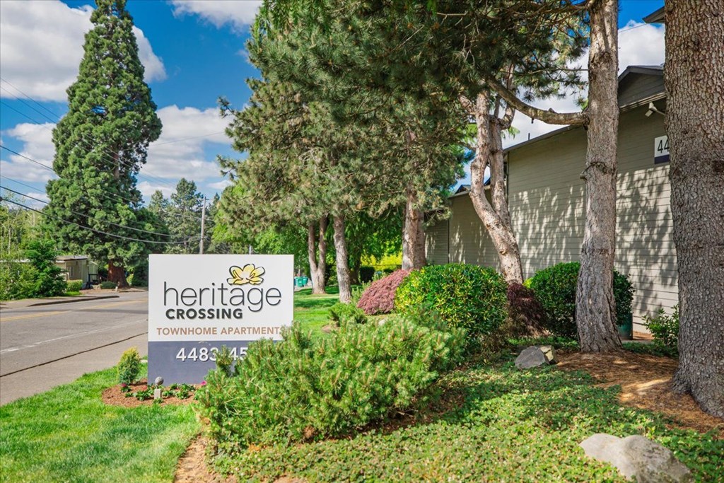A sign for Heritage Crossing Townhome Apartments is in front of a tree.