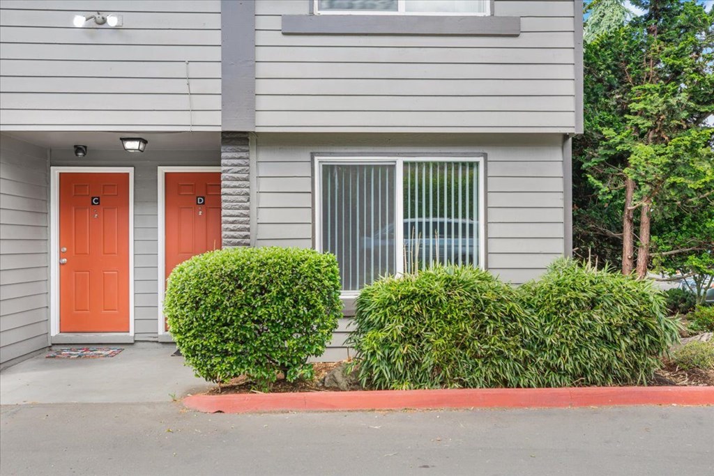A grey house with two orange doors and a red curb.