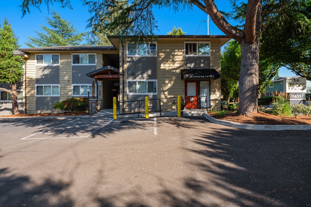 the front of a building with a parking lot and a tree