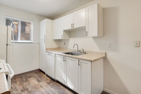 A kitchen with white cabinets and a wooden floor.