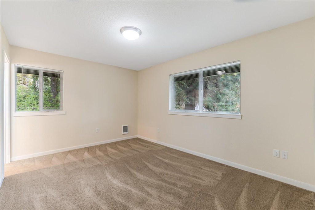A room with a carpeted floor and two windows.