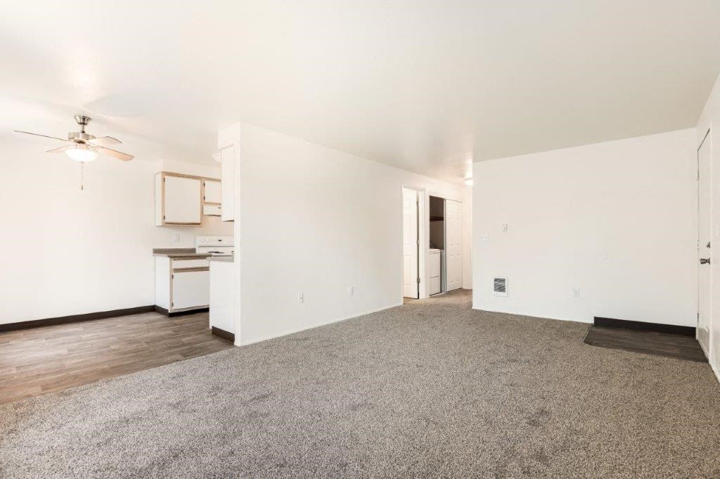 a living room with a ceiling fan and a kitchen in the background