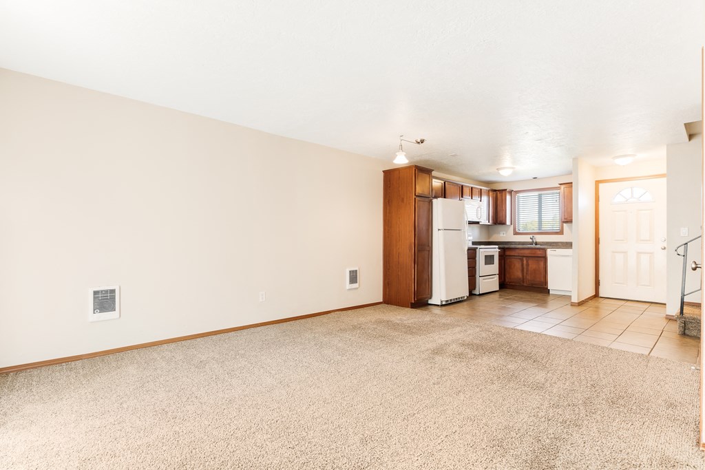 a living room with beige carpet and a kitchen in the background