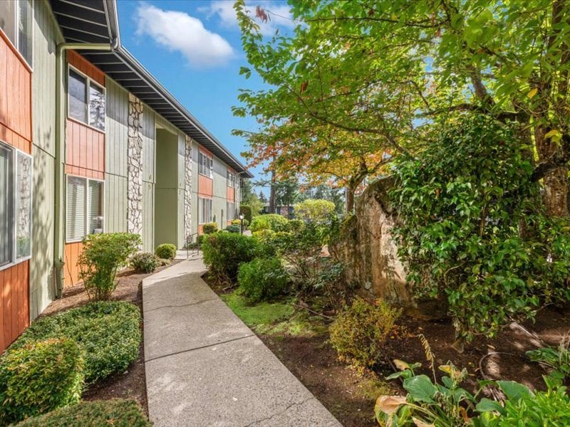 a sidewalk in front of a building with bushes and trees