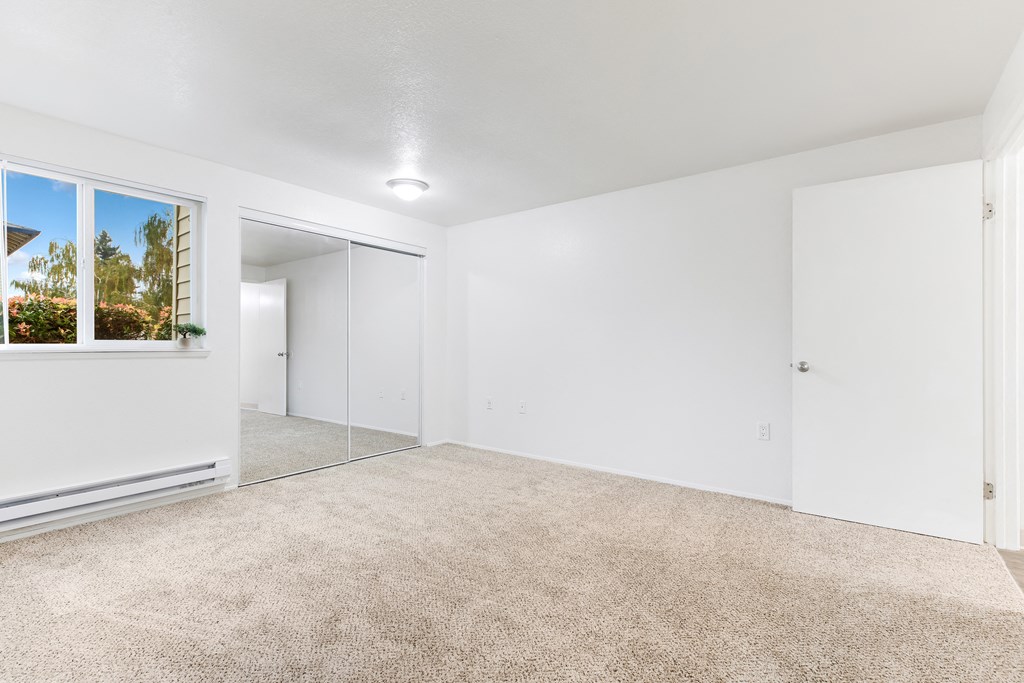 a spacious living room with white walls and carpeting and a large window