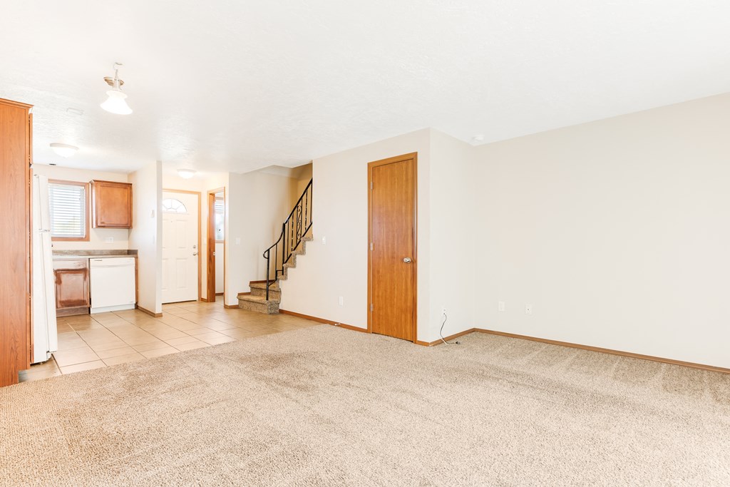 a living room with a beige rug and a kitchen in the background
