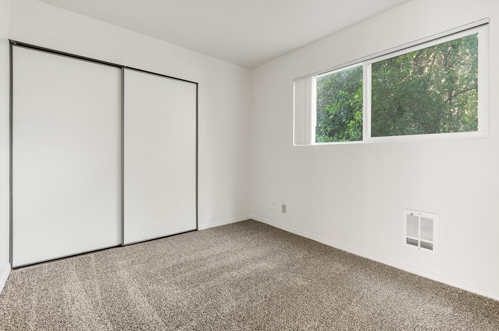 an empty room with carpet and white walls and a window