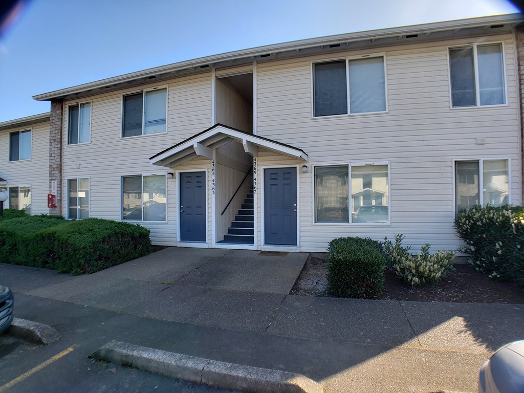 A beige apartment building with a blue door and stairs leading to the entrance.