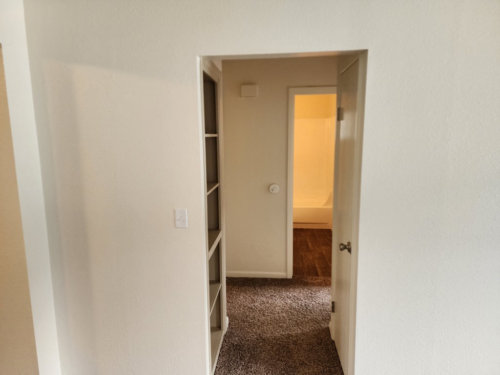 an empty room with a door open to a hallway and a door to a bedroom