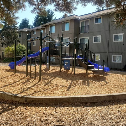 A playground with a slide and swings in front of a building.