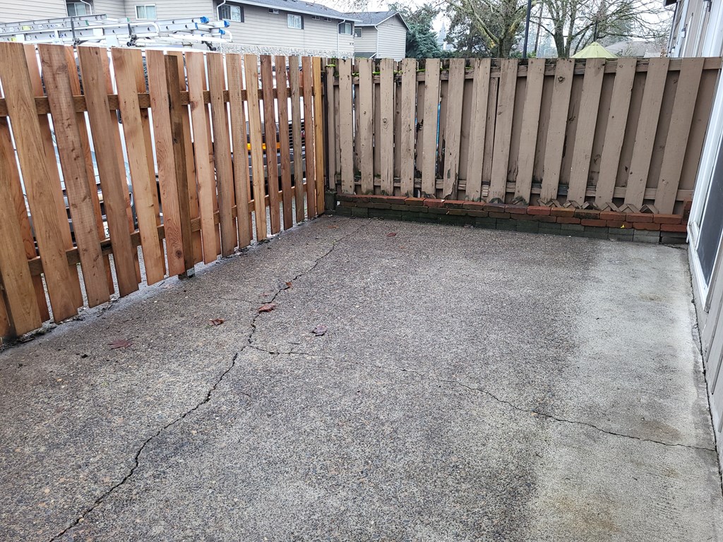 a backyard with a wooden fence and a concrete driveway