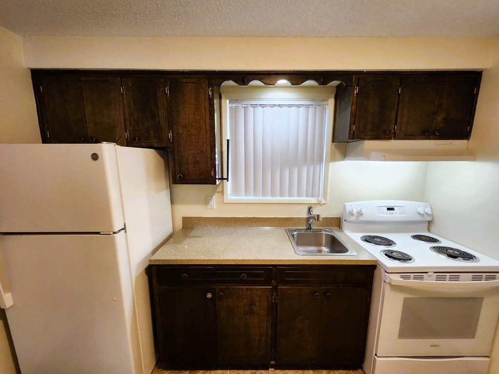Nell Anna Court small kitchen with a white fridge, a white stove, and brown cabinets.