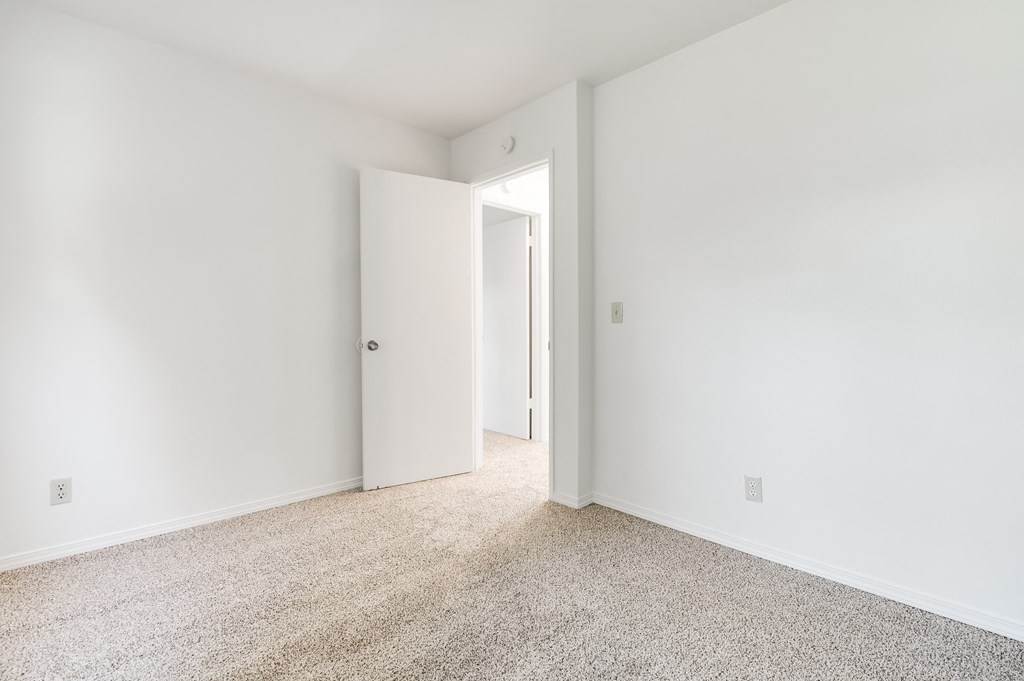 a bedroom with white walls and carpet and a door to a closet