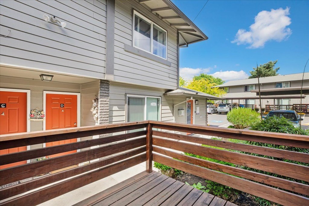 A wooden deck with a railing in front of a grey house with orange doors.