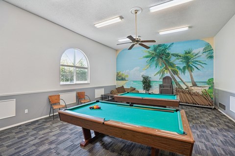 A pool table in a room with a mural of a beach scene on the wall.