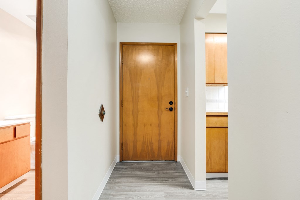 an empty room with a wooden door and a kitchen