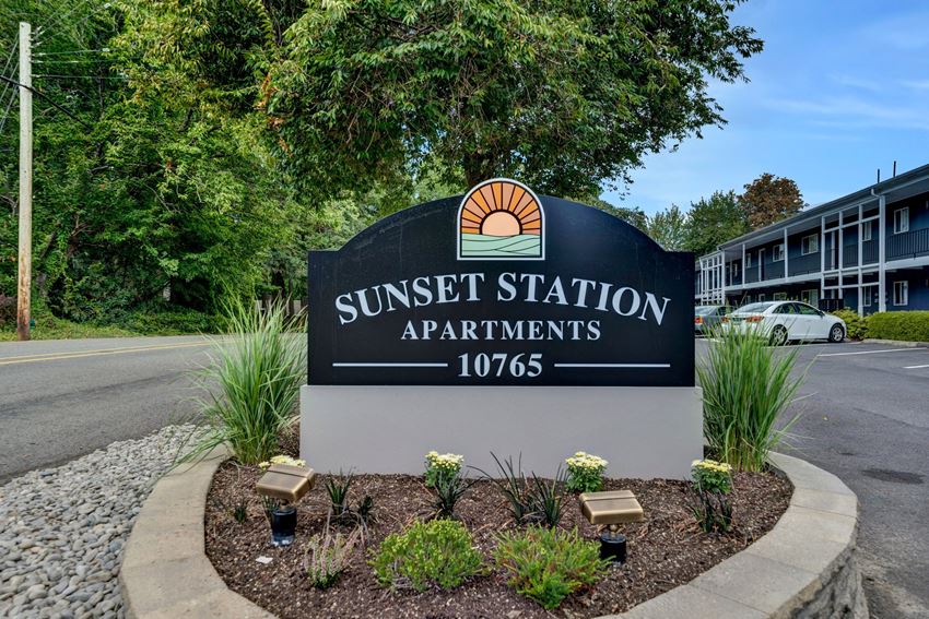 a sign for sunset station apartments with trees in the background